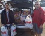 2 men holding plastic bags of groceries & lots of groceries in back of SUV